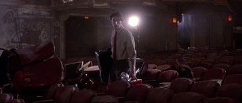Movie still from “Backdraft” (1991), directed by Ron Howard – A man in a suit and red tie standing in front of a pile of chairs; Wide shot, Low angle