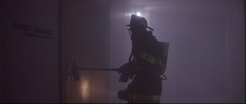 Movie still from “Backdraft” (1991), directed by Ron Howard – A fire fighter is standing in the smoke holding a fire axe; Medium shot, Low angle