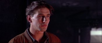Movie still from “Backdraft” (1991), directed by Ron Howard – A young man with long dark hair wearing a brown jacket; Close Up shot, Low angle