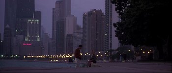 Movie still from “Backdraft” (1991), directed by Ron Howard – Two men sitting on a bench in front of a city skyline at night; Extreme Wide shot, High angle