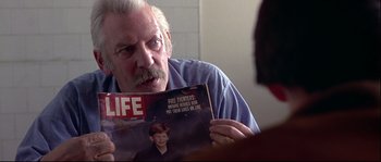 Movie still from “Backdraft” (1991), directed by Ron Howard – An older man reading a magazine in front of a bathroom mirror; Close Up shot, Over the shoulder angle