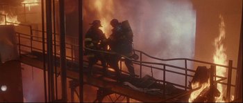 Movie still from “Backdraft” (1991), directed by Ron Howard – Two firemen are on a fire stair while a fire rages in the background; Wide shot, Low angle