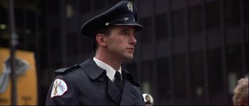 Movie still from “Backdraft” (1991), directed by Ron Howard – A man in a police uniform is standing in front of a building; Close Up shot, Low angle