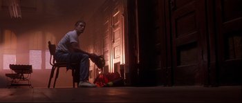 Movie still from “Backdraft” (1991), directed by Ron Howard – A man sitting on a chair in front of an open door; Wide shot, Low angle