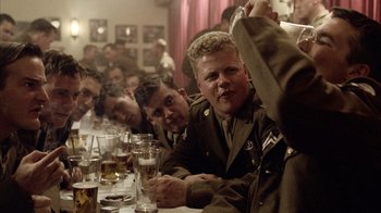 Movie still from “Band of Brothers” (2001), directed by David Frankel – A group of men sitting at a table with drinks in front of them; Medium shot, Over the shoulder angle
