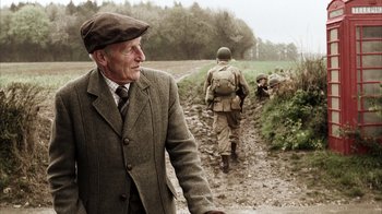 Movie still from “Band of Brothers” (2001), directed by David Frankel – An old man wearing a hat and a suit walking down a dirt road; Medium shot, Over the shoulder angle
