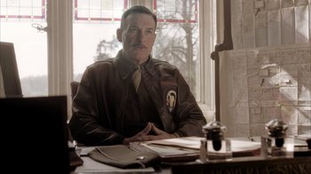 Movie still from “Band of Brothers” (2001), directed by David Frankel – A man sitting at a table in front of a stained glass window; Medium shot, Low angle