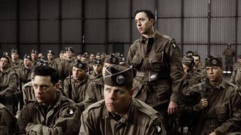 Movie still from “Band of Brothers” (2001), directed by David Frankel – A group of men in uniform sitting and standing in front of a wall; Medium shot, High angle