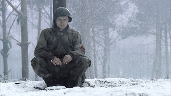 Movie still from “Band of Brothers” (2001), directed by David Frankel – A man sitting in the middle of a snow covered field; Medium shot, Low angle