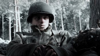 Movie still from “Band of Brothers” (2001), directed by David Frankel – A man wearing a helmet is sitting in the woods; Medium shot, High angle