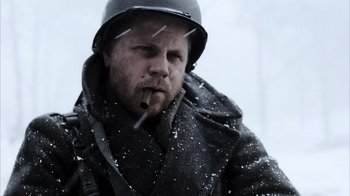 Movie still from “Band of Brothers” (2001), directed by David Frankel – A man wearing a helmet while smoking a cigarette in the snow; Close Up shot, Over the shoulder angle