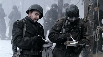 Movie still from “Band of Brothers” (2001), directed by David Frankel – Two men in uniforms are eating food in the snow; Medium shot, High angle