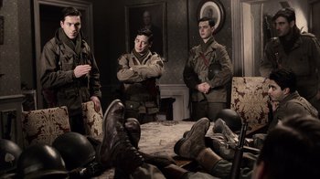 Movie still from “Band of Brothers” (2001), directed by David Frankel – A group of men standing in a room with their arms crossed; Medium shot, Low angle