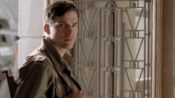 Movie still from “Band of Brothers” (2001), directed by David Frankel – A man standing in front of a wall with roman numerals on it; Close Up shot, Low angle