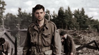 Movie still from “Band of Brothers” (2001), directed by David Frankel – A man in a military uniform standing next to another man; Medium shot, Low angle