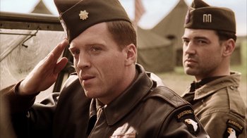 Movie still from “Band of Brothers” (2001), directed by David Frankel – A man in a military uniform saluting with another man in the background; Medium shot, Low angle