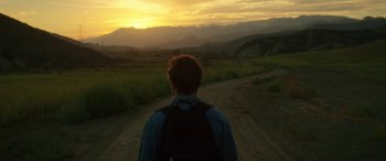 Movie still from “Band of Robbers” (2015), directed by Adam Nee – A man standing on the side of a dirt road at sunset; Wide shot, High angle