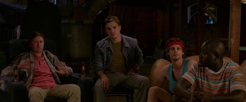 Movie still from “Band of Robbers” (2015), directed by Adam Nee – A man sitting on a chair next to two other people; Medium shot, Over the shoulder angle