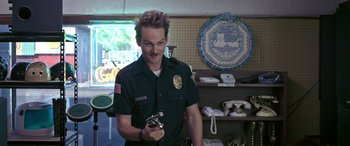 Movie still from “Band of Robbers” (2015), directed by Adam Nee – A police officer is holding something in his hand; Medium shot, Over the shoulder angle