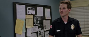 Movie still from “Band of Robbers” (2015), directed by Adam Nee – A police officer standing in front of a bulletin board; Close Up shot, Over the shoulder angle