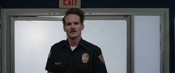 Movie still from “Band of Robbers” (2015), directed by Adam Nee – A man in a police uniform standing in front of a exit sign; Close Up shot, Over the shoulder angle