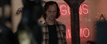 Movie still from “Band of Robbers” (2015), directed by Adam Nee – A man in a plaid shirt is standing in front of a neon sign; Medium shot, Over the shoulder angle