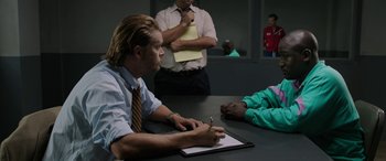 Movie still from “Band of Robbers” (2015), directed by Adam Nee – A man sitting at a table writing on a piece of paper; Medium shot, Over the shoulder angle