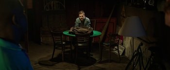 Movie still from “Band of Robbers” (2015), directed by Adam Nee – A man sitting at a table in a dark room; Wide shot, High angle