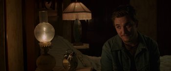 Movie still from “Band of Robbers” (2015), directed by Adam Nee – A man sitting on a bed next to a lamp; Medium shot, Over the shoulder angle