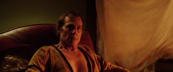 Movie still from “Band of Robbers” (2015), directed by Adam Nee – An older man sitting in a chair in a dark room; Close Up shot, Low angle