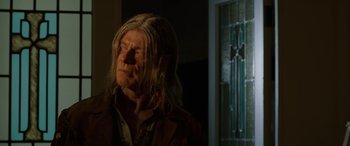 Movie still from “Band of Robbers” (2015), directed by Adam Nee – A man with long hair is standing in a dark room; Close Up shot, Low angle