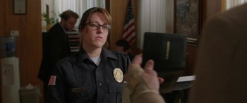 Movie still from “Band of Robbers” (2015), directed by Adam Nee – A police officer is holding a book in her hand; Close Up shot, Over the shoulder angle