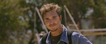 Movie still from “Band of Robbers” (2015), directed by Adam Nee – A man with a beard and a jacket on smiling for the camera; Close Up shot, Over the shoulder angle