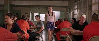 Movie still from “Band of Robbers” (2015), directed by Adam Nee – A woman in a pink shirt and blue skirt standing in front of a group of people; Medium shot, Over the shoulder angle