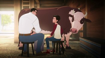 Movie still from “Batman and Superman: Battle of the Super Sons” (2022), directed by Matt Peters – A man and a boy sitting on stools next to a brown cow; Wide shot, High angle