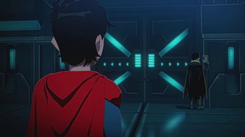 Movie still from “Batman and Superman: Battle of the Super Sons” (2022), directed by Matt Peters – A man wearing a red and blue cape looking into a room; Wide shot, Over the shoulder angle