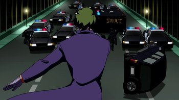 Movie still from “Batman: Death in the Family” (2020), directed by Brandon Vietti – A man in a purple suit is riding a bike down the street; Wide shot, Over the shoulder angle