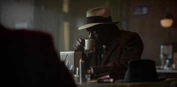 Movie still from “Fargo” (2014), created by Noah Hawley – A man in a hat drinking a cup of coffee; Medium shot, Over the shoulder angle