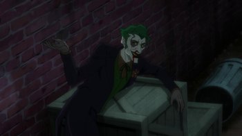 Movie still from “Batman: Hush” (2019), directed by Justin Copeland – The joker is sitting on a crate in a dark room; Medium shot, High angle