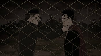 Movie still from “Batman: The Killing Joke” (2016), directed by Sam Liu – Two men are standing next to each other in front of a wire fence; Medium shot, Over the shoulder angle