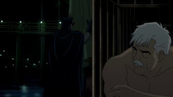 Movie still from “Batman: The Killing Joke” (2016), directed by Sam Liu – A man sitting in front of another man in a dark room; Medium shot, Over the shoulder angle