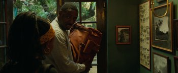 Movie still from “Beast” (2022), directed by Baltasar Kormákur – A man holding a brown bag in front of a window; Close Up shot, Over the shoulder angle
