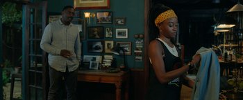 Movie still from “Beast” (2022), directed by Baltasar Kormákur – A man and a woman standing in front of a table; Medium shot, Over the shoulder angle