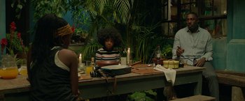 Movie still from “Beast” (2022), directed by Baltasar Kormákur – A person sitting at a table with a plate of food; Medium shot, Over the shoulder angle
