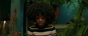 Movie still from “Beast” (2022), directed by Baltasar Kormákur – A young girl with a large afro in a striped sweater; Close Up shot, Over the shoulder angle