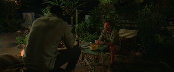 Movie still from “Beast” (2022), directed by Baltasar Kormákur – A man sitting at an outdoor table with a bottle of wine; Wide shot, Over the shoulder angle