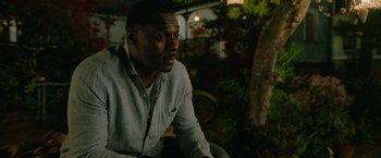 Movie still from “Beast” (2022), directed by Baltasar Kormákur – A man sitting on a chair in a yard; Close Up shot, Over the shoulder angle