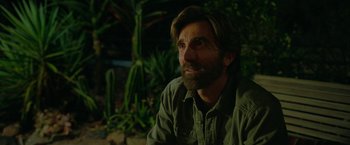 Movie still from “Beast” (2022), directed by Baltasar Kormákur – A man with a beard sitting in front of some plants; Close Up shot, Over the shoulder angle
