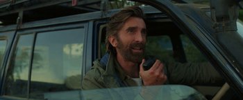 Movie still from “Beast” (2022), directed by Baltasar Kormákur – A man with long hair and a goatee is holding a cell phone; Close Up shot, Over the shoulder angle