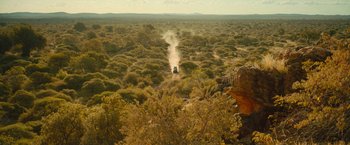 Movie still from “Beast” (2022), directed by Baltasar Kormákur – An aerial view of a dirt field with a train coming up the hill; Extreme Wide shot, High angle
